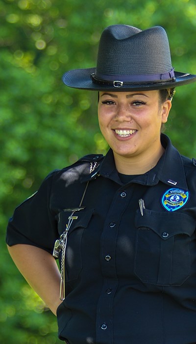 Female corrections officer smiling at camera with trees in the background.