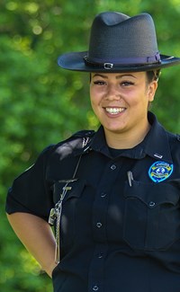 Female corrections officer smiling at camera with trees in the background.